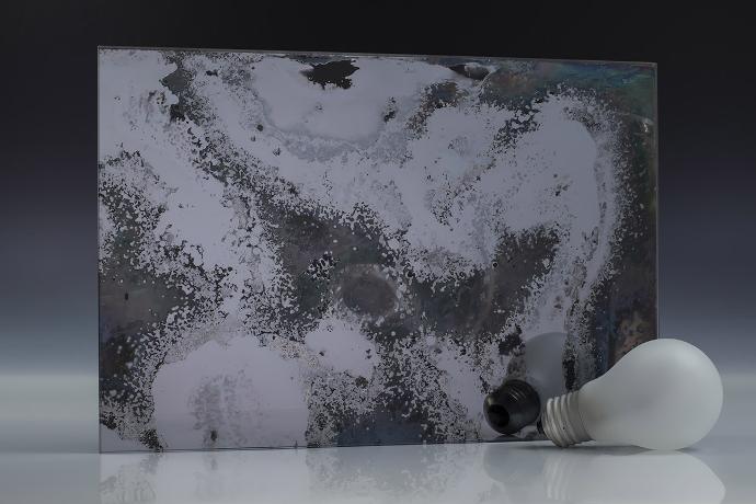 Double galena oxide - galena - antique mirror - sample A square piece of gray mirror with a pronounced patina and a light bulb on a neutral background