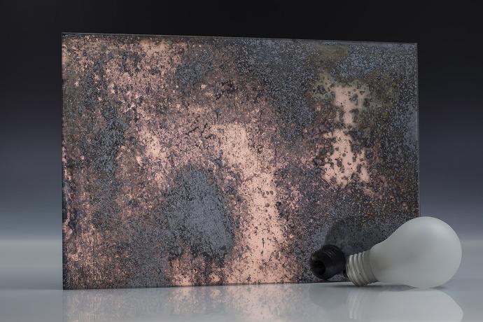Heavy copper oxide - copper - antique mirror - sample A square piece of copper mirror with dark spots and a light bulb on a neutral background