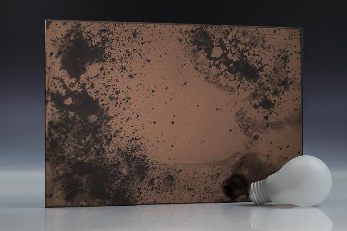 Deep copper oxide - copper - antique mirror - sample A square piece of copper mirror with dark spots and a light bulb on a neutral background