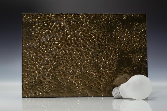Dark gold - metallic - reljefno staklo - uzorak Četverokutni komad reljefnog stakla tamne boje i žarulja na neutralnoj pozadini