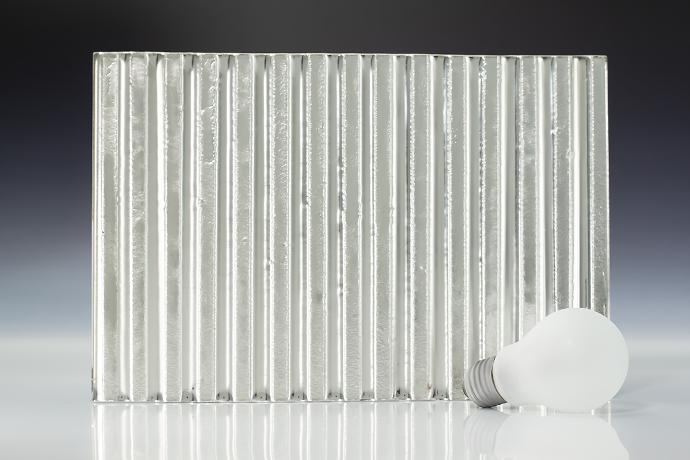 Intaglio ribbed silver - metallic - reljefno staklo - uzorak Četverokutni komad reljefnog stakla srebrne boje i žarulja na neutralnoj pozadini