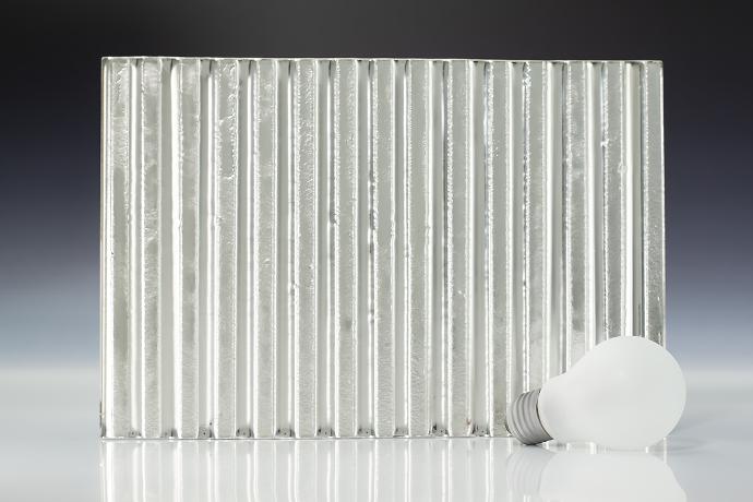 A square piece of texture silver colored glass and light bulb on a neutral background