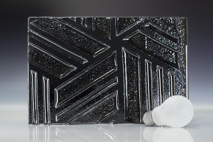 Intaglio galena space - metallic - reljefno staklo - uzorak Četverokutni komad reljefnog stakla tamne boje i žarulja na neutralnoj pozadini