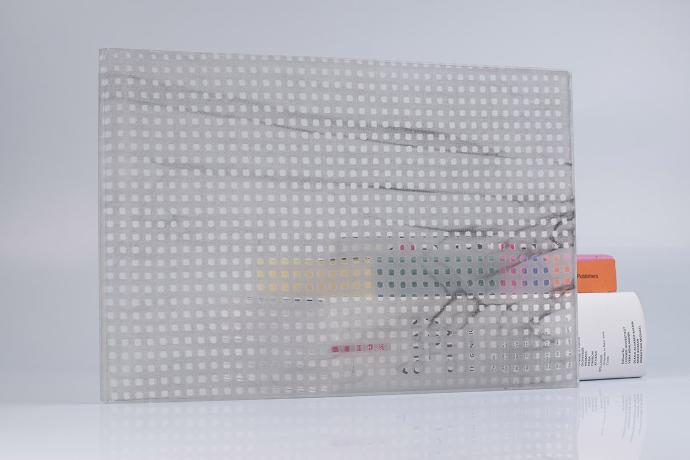 A square piece of glass with grey textiles and books on a neutral background