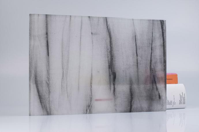 A square piece of glass with grey textiles and books on a neutral background