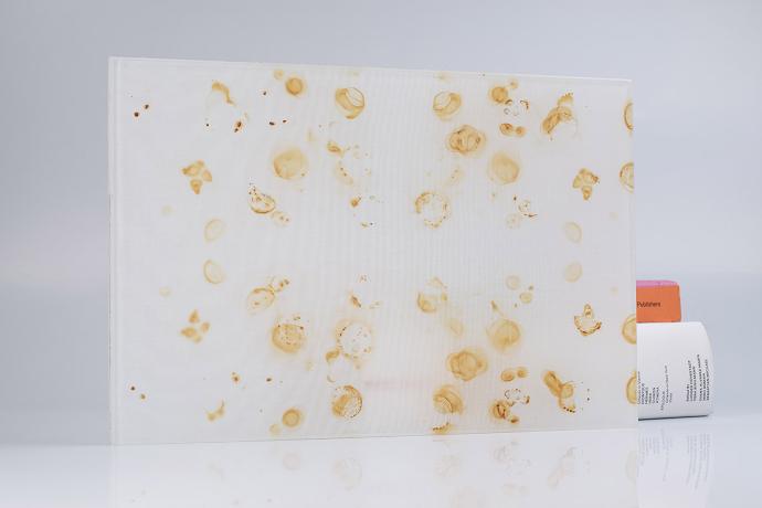 A square piece of glass with white textile and rust spots and books on a neutral background