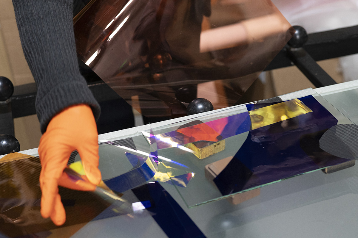 A hand in a protective glove, a plate of glass and different foils.