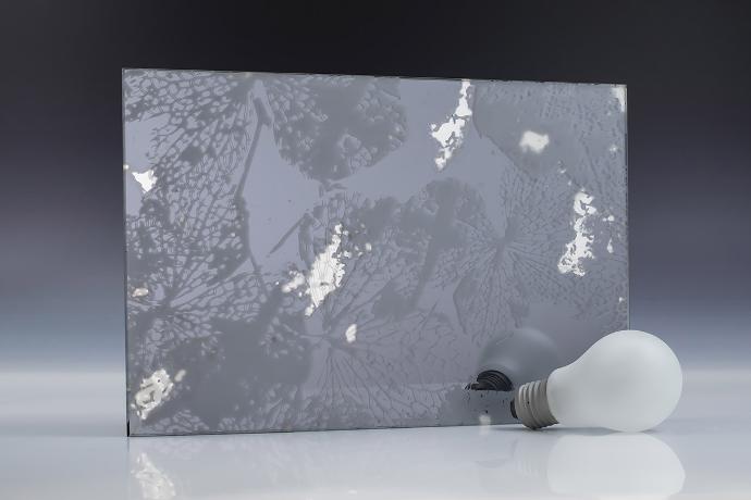 A square piece of etch glass with a floral pattern, a light bulb and books on a neutral background