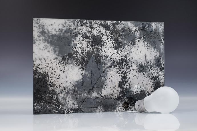 Četverokutni komad pjeskarenog ogledala s floralnim uzorkom i žarulja na neutralnoj pozadini