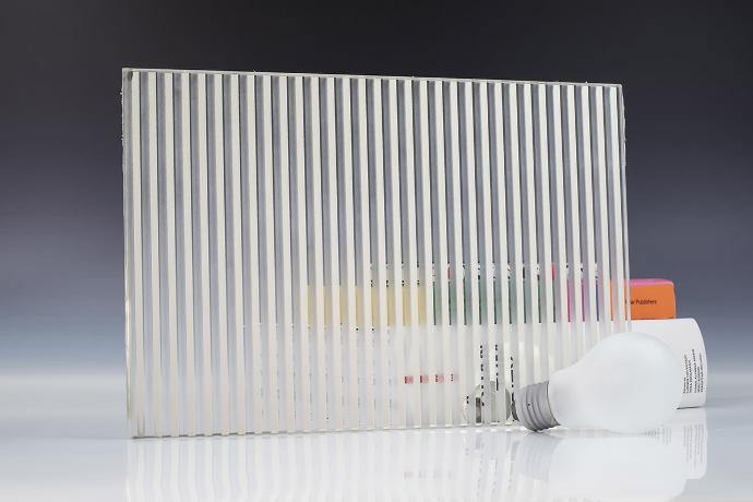 A square piece of etch mirror with a linear pattern, a light bulb and books on a neutral background