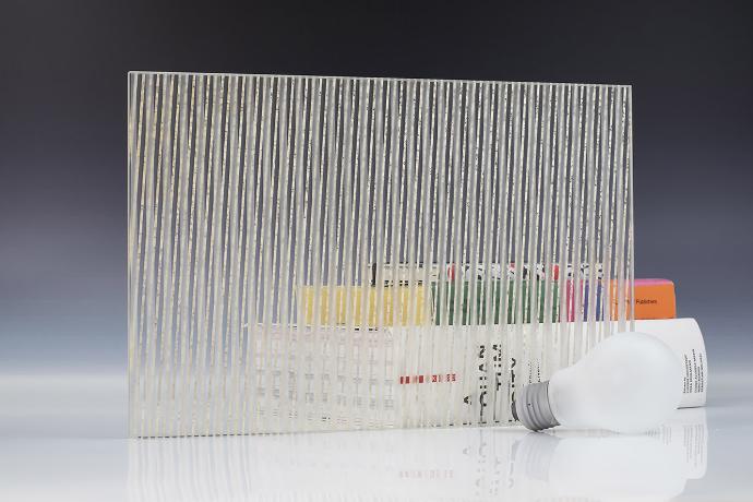 A square piece of etch mirror with a linear pattern, a light bulb and books on a neutral background