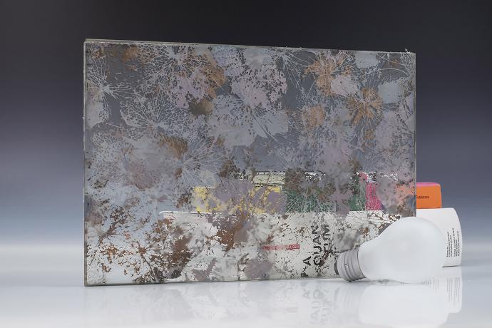 Četverokutni komad pjeskarenog stakla s floralnim uzorkom, žarulja i knjige na neutralnoj pozadini
