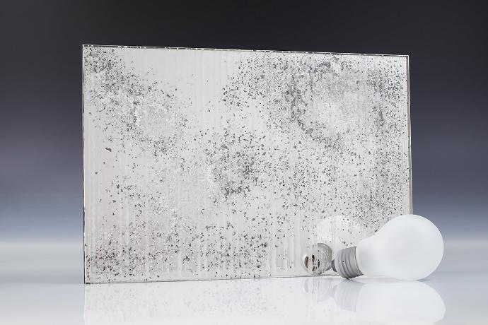 A square piece of patterned etch mirror, a light bulb and books on a neutral background