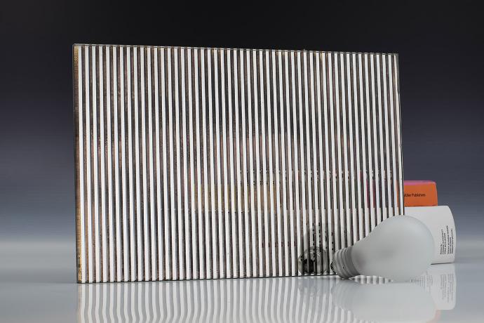 A square mirror piece with a linear pattern, a light bulb and books on a neutral background