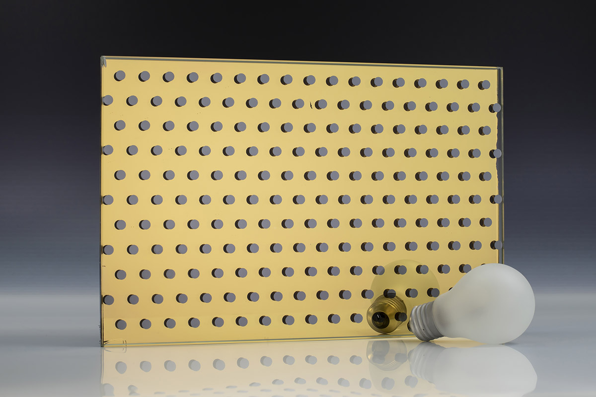 A square piece of gold mirror with a dot pattern and a light bulb on a neutral background
