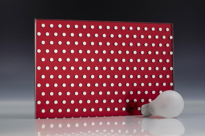 A square piece of red mirror with a dot pattern and a light bulb on a neutral background