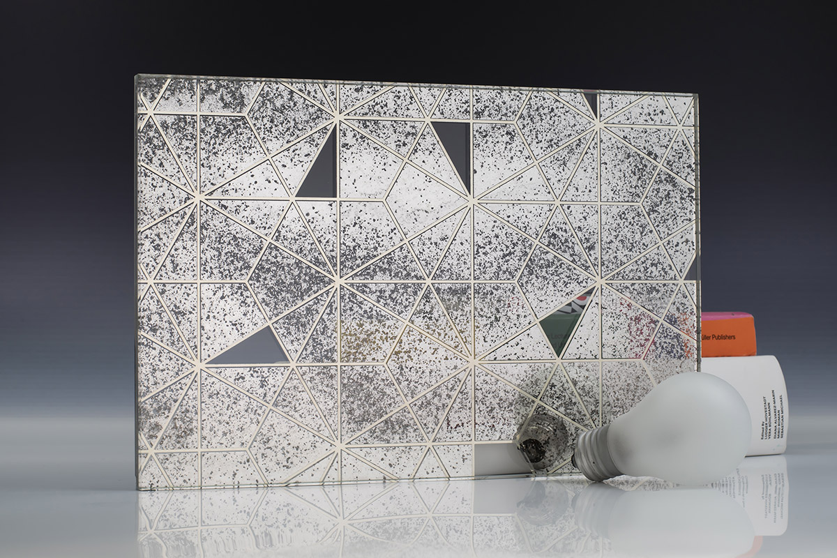 A square piece of silver mirror with a hexagon pattern, light bulbs and books on a neutral background