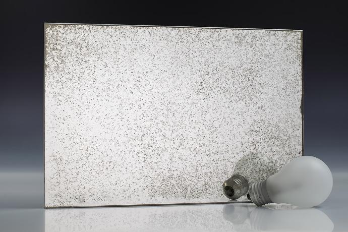 A square piece of mirror with a patina effect and light bulbs on a neutral background